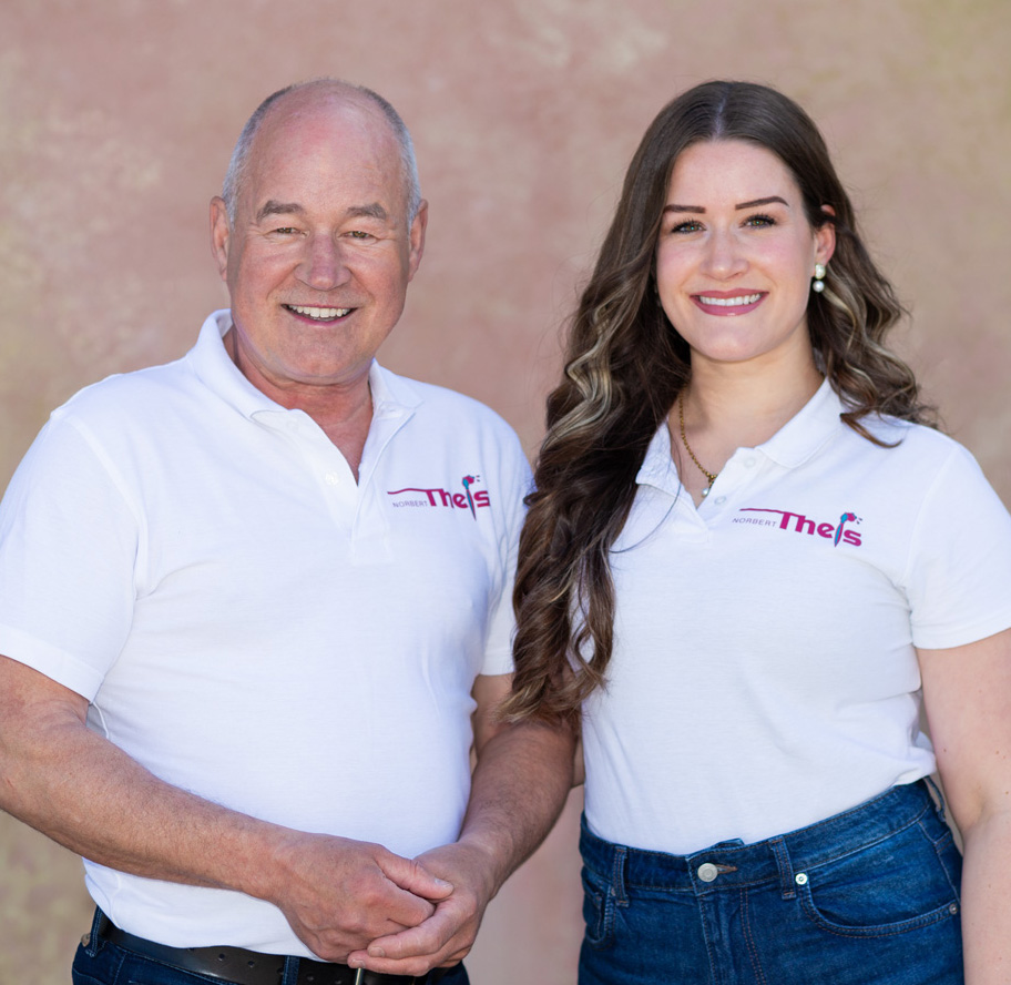 Norbert Theis und Danielle Theis, zwei Generationen des Familienunternehmens Maler Theis, in Firmenkleidung vor hellem Hintergrund.